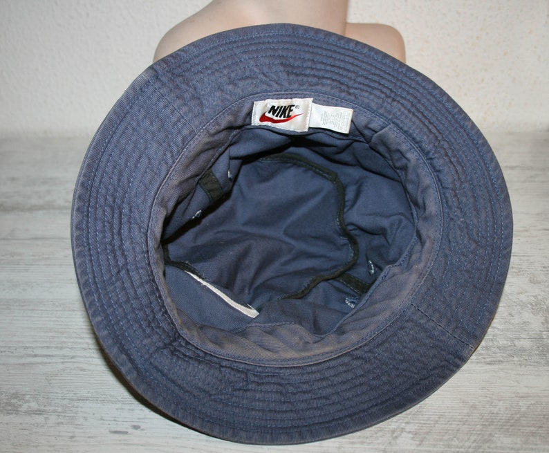 May include: A blue bucket hat with a Nike logo on the front. The hat is made of a soft, cotton fabric and has a wide brim.