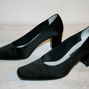 K&ouml;nnte beinhalten: Ein Paar schwarze Satin-Pumps mit quadratischer Spitze und Blockabsatz.