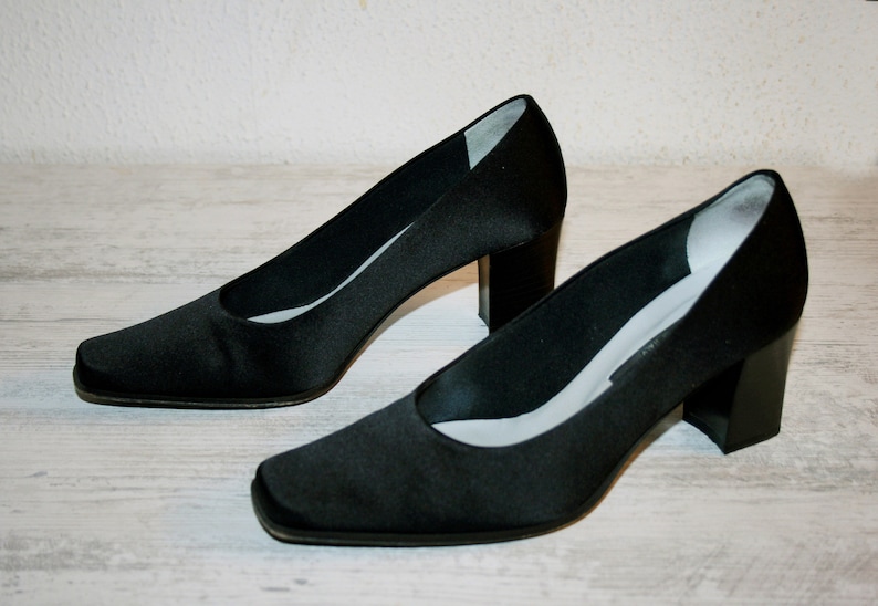 K&ouml;nnte beinhalten: Ein Paar schwarze Satin-Pumps mit quadratischer Spitze und Blockabsatz.