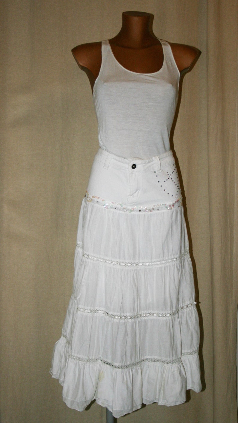 May include: White tiered skirt with a white tank top. The skirt has a denim waistband with embellishments.