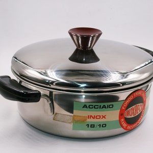 Può includere: Una pentola in acciaio inox con un manico nero e una manopola rossa sul coperchio. La pentola ha un'etichetta che recita "Acciaio Inox 18/10" e "Fondo Trimetalico Inoxbec Rame Incorporato".