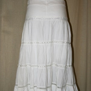 May include: A white tiered skirt with lace trim. The skirt is made of a lightweight fabric and has a flowy silhouette.