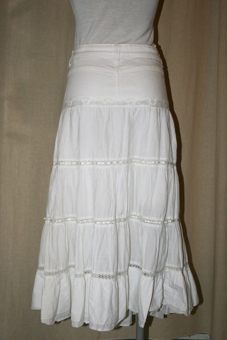 May include: A white tiered skirt with lace trim. The skirt is made of a lightweight fabric and has a flowy silhouette.