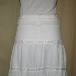 May include: A white tiered skirt with lace trim. The skirt is made of a lightweight fabric and has a flowy silhouette.