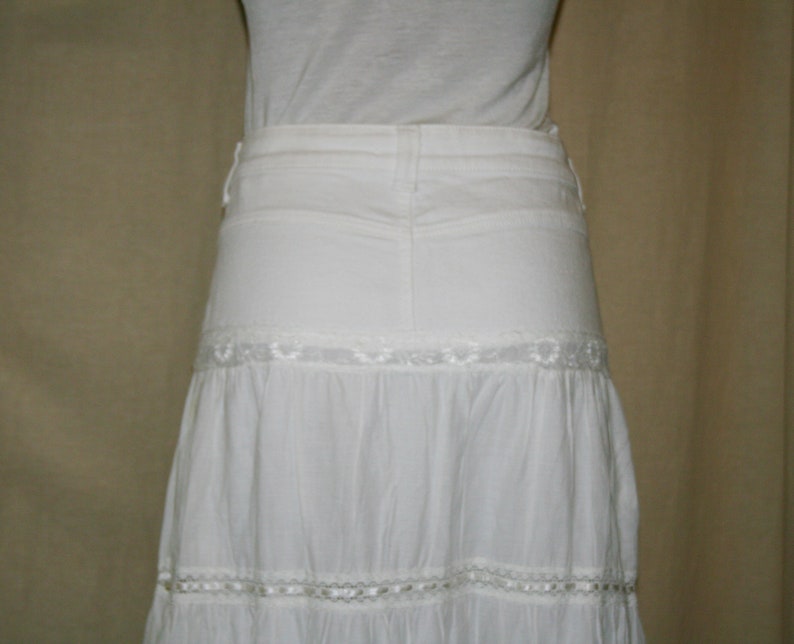 May include: A white tiered skirt with lace trim. The skirt is made of a lightweight fabric and has a flowy silhouette.