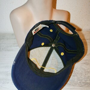 Pu&ograve; includere: Un cappello da baseball in rete blu e giallo con un logo Nike sul retro. Il cappello ha dettagli di cucitura gialli e un cinturino regolabile giallo.