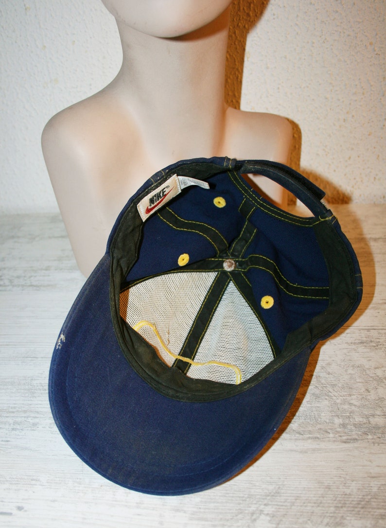 Pu&ograve; includere: Un cappello da baseball in rete blu e giallo con un logo Nike sul retro. Il cappello ha dettagli di cucitura gialli e un cinturino regolabile giallo.