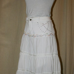 May include: White tiered skirt with a white tank top. The skirt has a beaded design on the waistband.