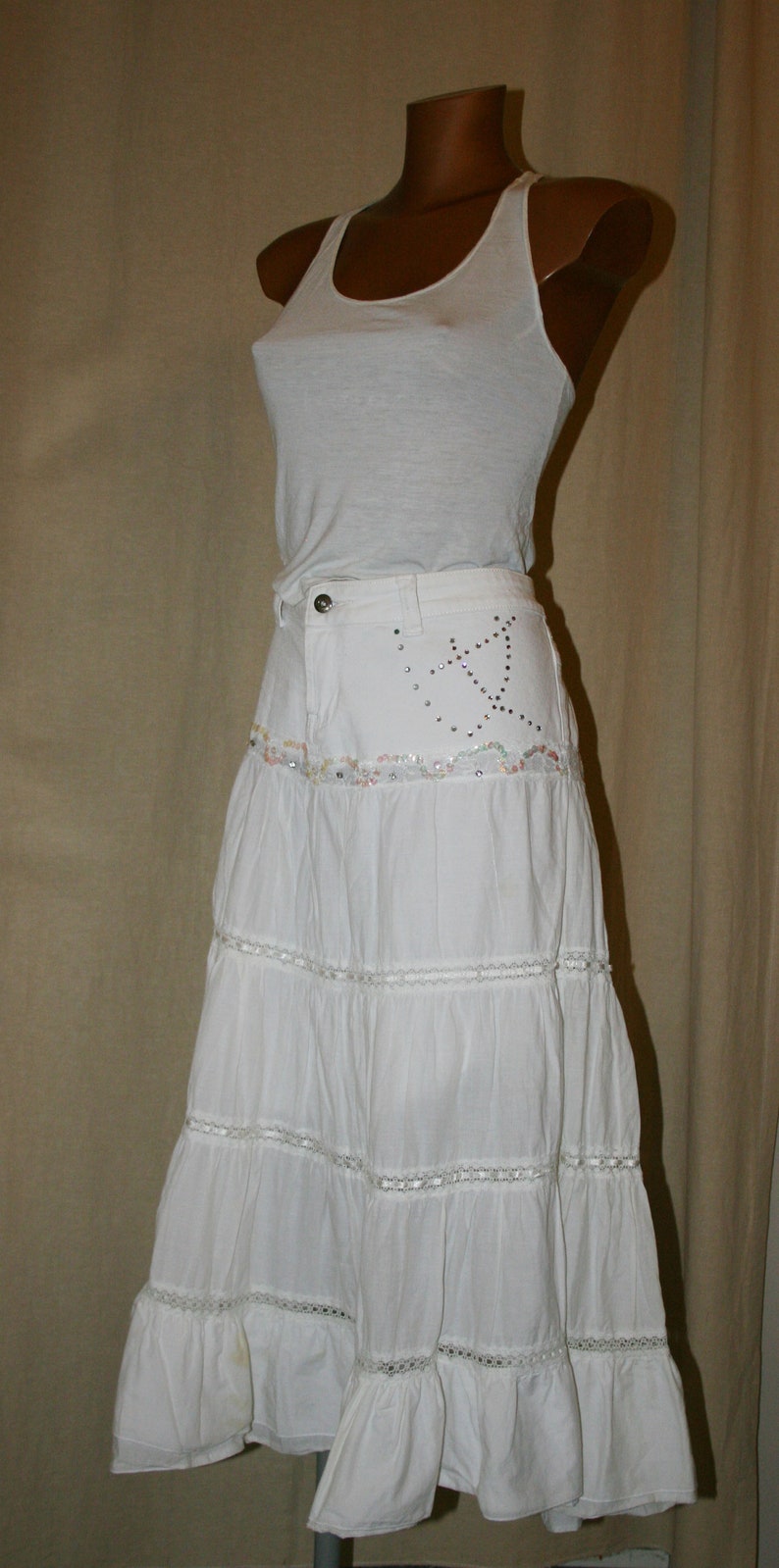 May include: White tiered skirt with a white tank top. The skirt has a beaded design on the waistband.
