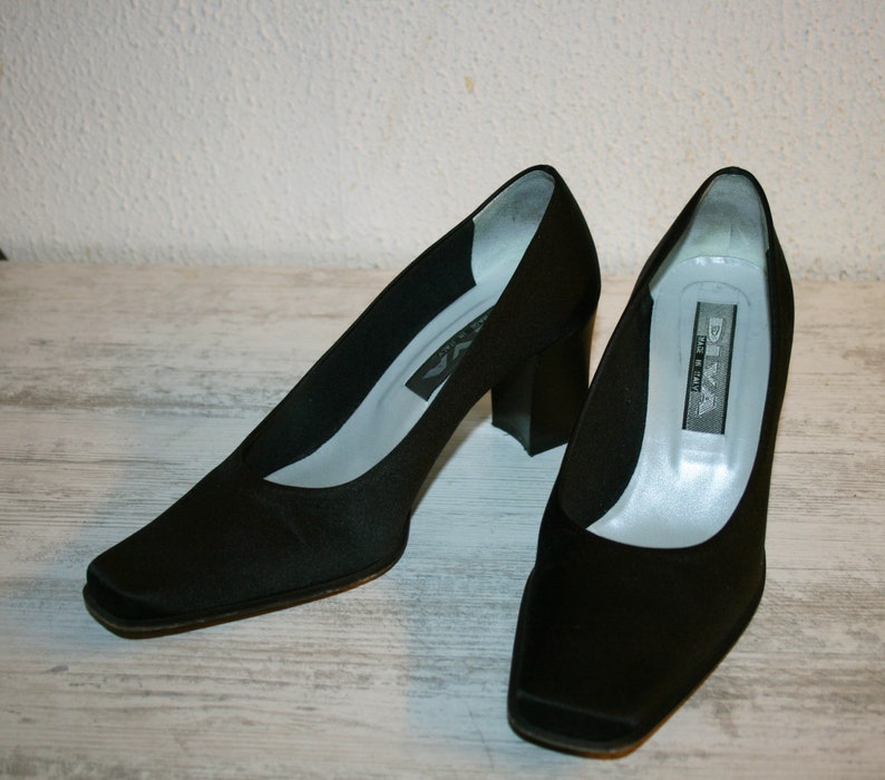 K&ouml;nnte beinhalten: Ein Paar schwarze Satin-Pumps mit quadratischer Spitze und Blockabsatz. Die Schuhe sind von der Marke "Diva" und wurden in Italien hergestellt.