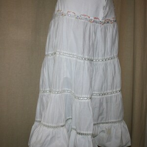 May include: A white tiered maxi skirt with a lace trim and beaded embellishment around the waist.