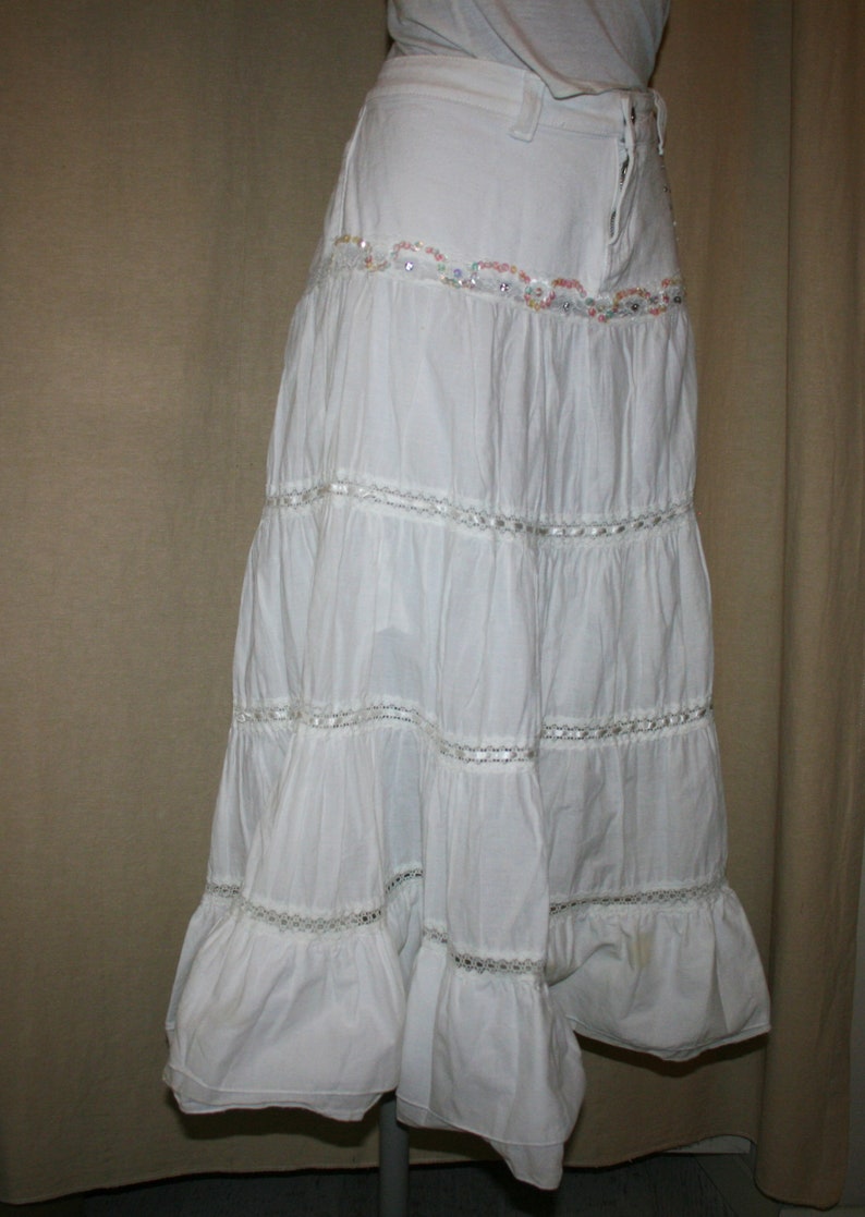 May include: A white tiered maxi skirt with a lace trim and beaded embellishment around the waist.