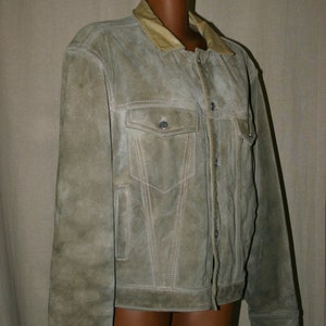May include: A light brown suede jacket with a tan collar and button closure. The jacket has two flap pockets on the front and two side pockets.