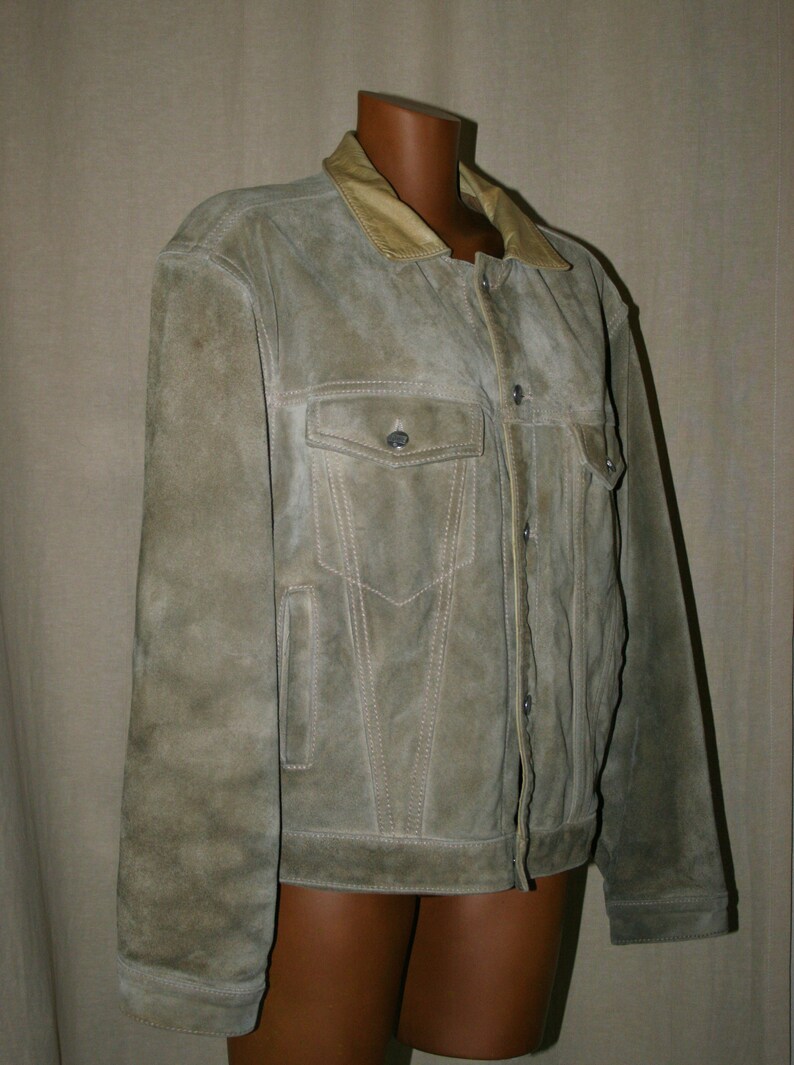 May include: A light brown suede jacket with a tan collar and button closure. The jacket has two flap pockets on the front and two side pockets.