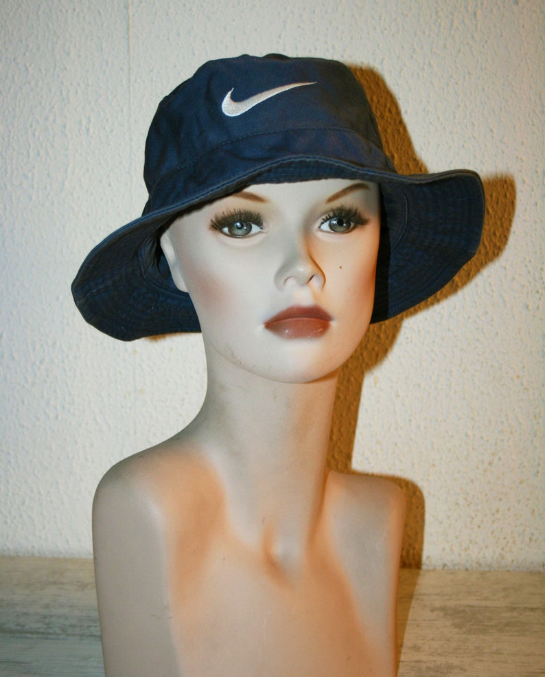 May include: A blue bucket hat with a white Nike swoosh logo. The hat is on a mannequin head.