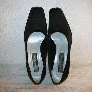 K&ouml;nnte beinhalten: Ein Paar schwarze Satin-Pumps mit spitzer Zehenpartie und niedrigem Absatz. Die Schuhe haben ein silbernes Futter und der Markenname "DIVA" ist auf der Innensohle aufgedruckt.