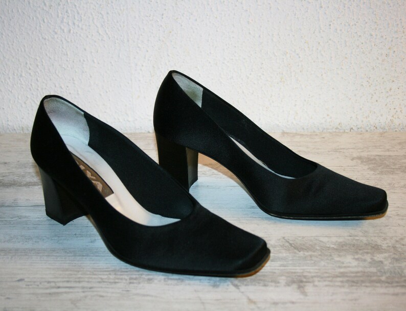K&ouml;nnte beinhalten: Ein Paar schwarze Satin-Pumps mit quadratischer Spitze und Blockabsatz.