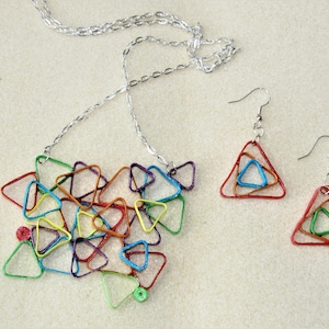May include: A colorful necklace and earrings set made of layered paper triangles. The necklace is silver chain with a pendant of multi-colored triangles. The earrings are silver hooks with a pendant of multi-colored triangles.