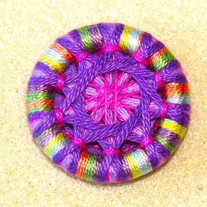 May include: A colorful, handmade button with a purple, pink, and green striped outer ring and a purple and pink center.