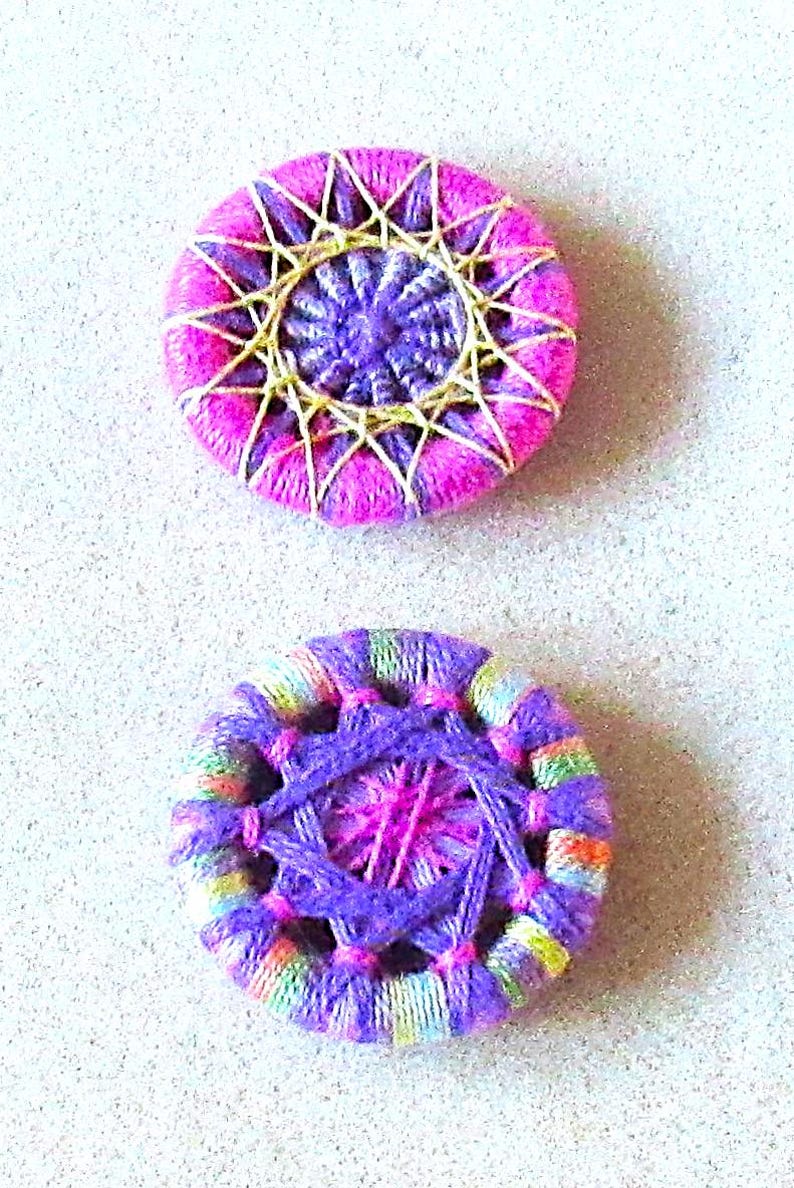 May include: Two handmade yarn buttons, one with a pink and white starburst pattern and the other with a purple and multi-colored striped pattern.