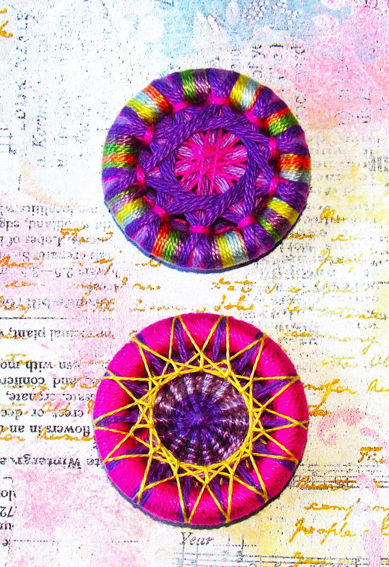 May include: Two colorful crocheted buttons with a purple center and a pink inner circle. The buttons are surrounded by a multi-colored yarn with yellow, green, blue, and pink accents.