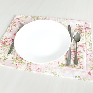 May include: A white plate with a fork, knife, and spoon on a pink floral placemat.