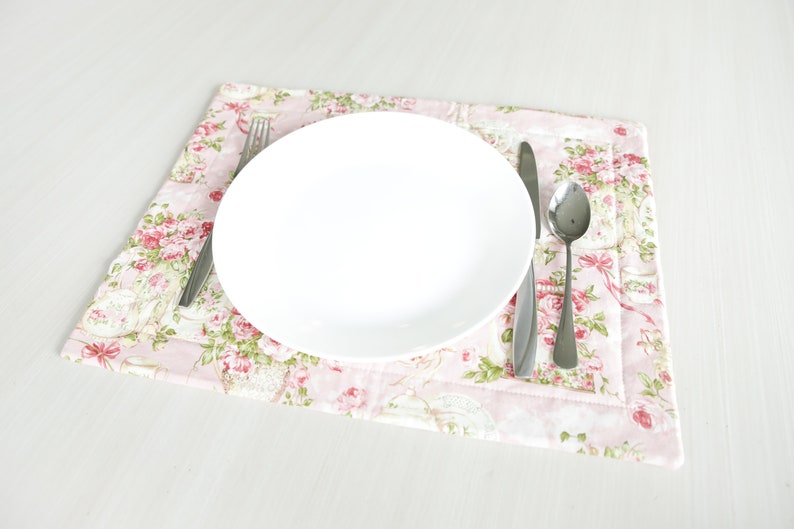 May include: A white plate with a fork, knife, and spoon on a pink floral placemat.