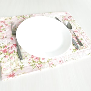 May include: A white ceramic plate with a silver fork and spoon on a pink floral placemat.