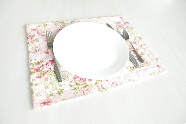 May include: A white ceramic plate with a silver fork and spoon on a pink floral placemat.