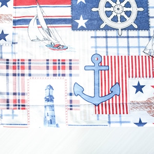 May include: A white fabric with a nautical theme featuring a red, white, and blue color scheme. The fabric has a patchwork design with various nautical elements, including a sailboat, an anchor, a ship's wheel, and a lighthouse.