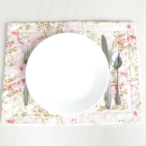 May include: A white ceramic plate with a silver fork, knife, and spoon on a pink floral placemat.