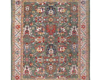 May include: A rectangular, hand-knotted rug with a central field of muted green. The rug features an intricate floral pattern in red, blue, yellow, and cream, framed by a detailed border. The rug's design is traditional, with a distressed look.