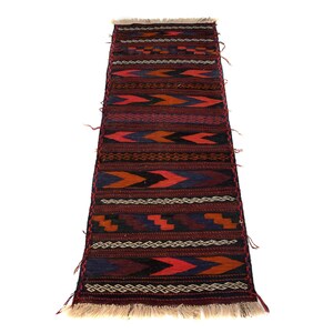 May include: A rectangular, hand-woven rug with a repeating geometric pattern in shades of red, blue, orange, and white. The rug has a fringed edge and is likely made of wool or a similar material. The design features arrow and zig-zag motifs.