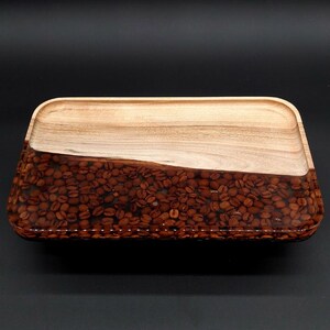 May include: Rectangular wooden tray with a diagonal design. The top half is light-coloured wood, while the bottom half is filled with coffee beans encased in clear resin. The tray has rounded corners and a stitched border.