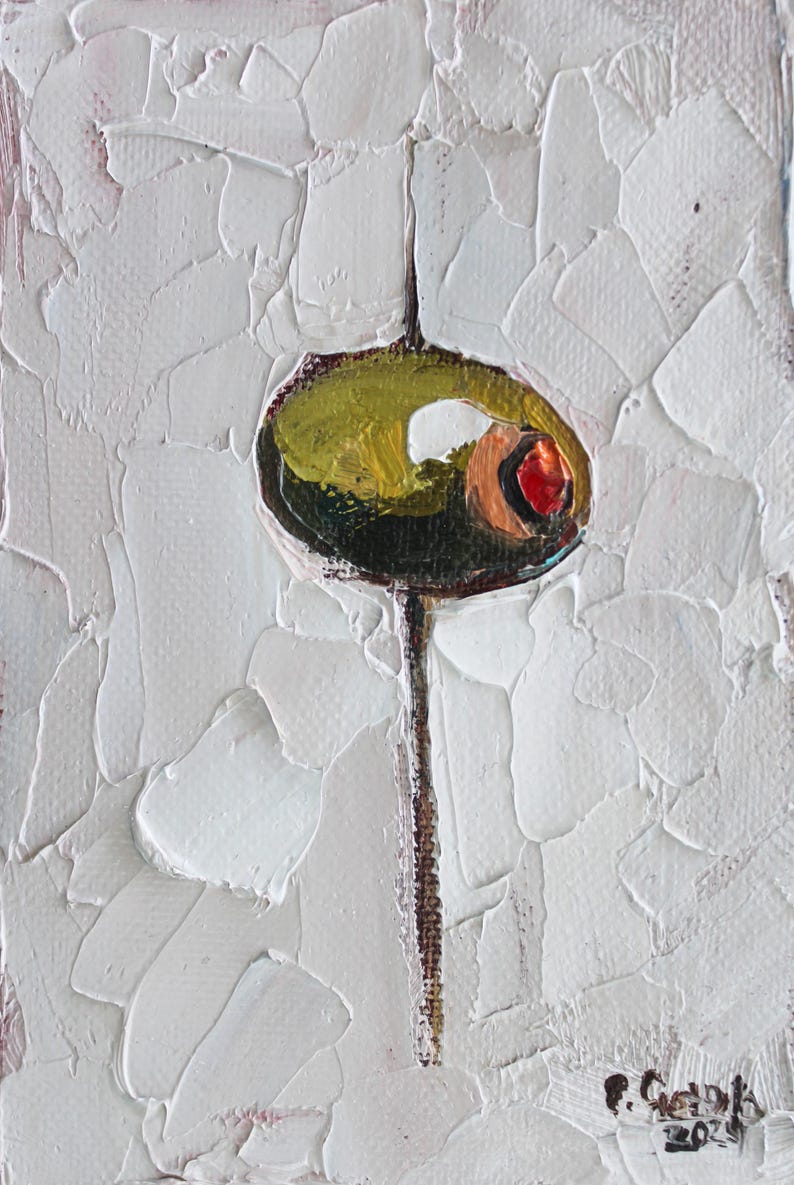 May include: An oil painting on canvas featuring a single green olive with a red pimento center, skewered on a thin vertical stick. The background consists of thick, textured white impasto paint strokes. A signature and the year 2024 appear at the bottom.