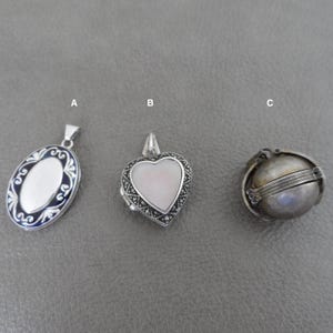 May include: Three silver locket pendants. The first is oval shaped with blue enamel and white interior. The second is a heart shaped locket with a pink interior and black markings. The third is a round locket with a hinged lid.