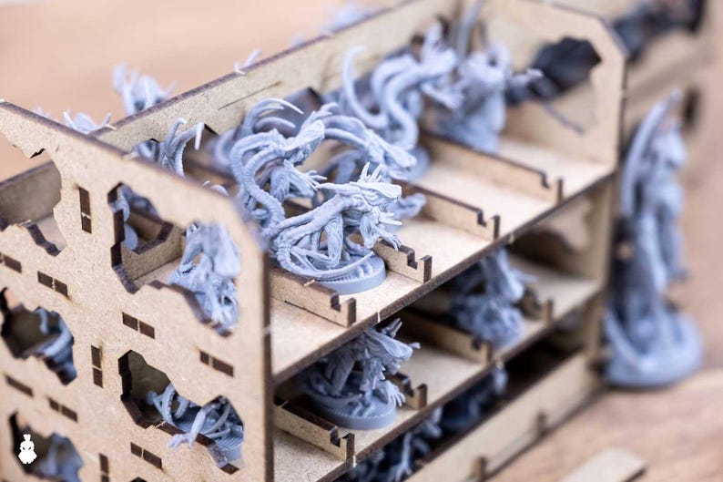 May include: A wooden organizer filled with gray miniature figures. The organizer has multiple shelves and cut-out designs. The figures appear to be fantasy creatures with tentacles and other otherworldly features. The overall theme suggests a tabletop gaming accessory.