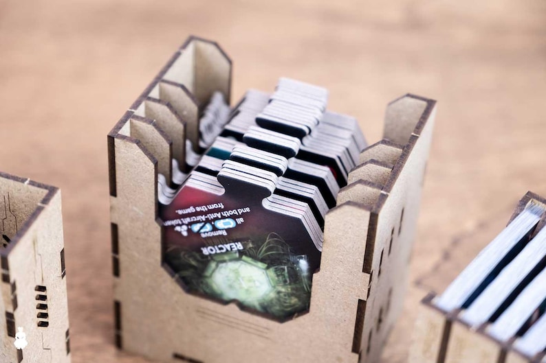 May include: Wooden game card holders filled with game cards. The holders are made of light brown wood and have a slotted design. The cards have a black and white design with some color accents and text. The text on the cards reads "REACTOR".