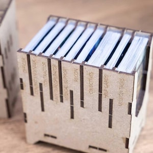 May include: Two wooden card holders with laser-cut labels. The labels include "Officer", "Combat Engineer", "Contractor", "Heavy Gun Operator", "Medical Support", "Recon", "Objectives", "Help Cards", and "Mission Tasks". The holders contain stacks of cards.