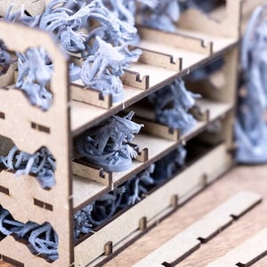 May include: A wooden organizer with multiple shelves, filled with gray miniature figurines. The organizer has cut-out shapes and is designed to hold the figurines. The figurines appear to be fantasy or sci-fi themed.