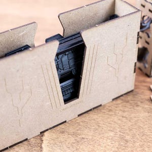 May include: A set of unfinished wooden card holders, with the text "CARD HOLDERS" visible. The holders are designed with a geometric aesthetic and feature cut-out designs. Other components and miniatures are also present.