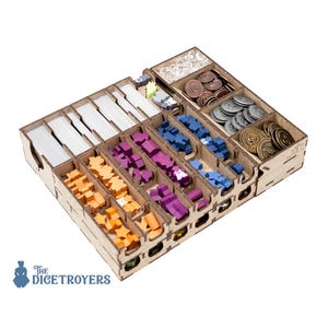 May include: A wooden board game organiser with various compartments containing game pieces. The compartments hold stacks of cards, orange, purple, and blue game pieces, and coins. The organiser is made of light brown wood and is designed to hold board game components.