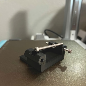 May include: A black 3D printed clamp with a silver metal rod and a nut. The clamp has two holes on the side.