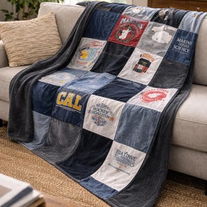 May include: A patchwork throw blanket with a variety of patches in shades of blue, gray, and white. The blanket is draped over a gray sofa and features text and graphics on the patches, including "CAL" and "MARINE SCIENCE".