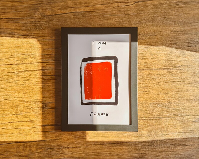 Op de afbeelding: Een zwart ingelijst afdruk met de tekst "I AM A FRAME" en een rood vierkant in een zwart kader.