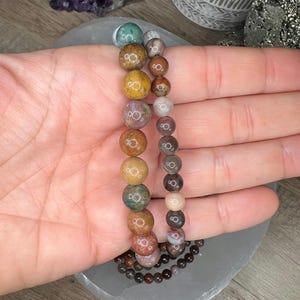 May include: Two bracelets made of colorful agate beads. The beads are round and have a variety of colors, including brown, red, green, and yellow. The bracelets are stacked on top of each other.