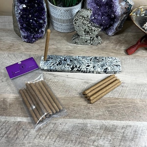 May include: A set of brown incense sticks in a clear plastic bag with a label that reads "House Alchemy" and a black and white marble incense holder with a single incense stick standing upright.