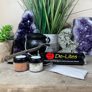 May include: A black cast iron cauldron with a metal handle, a pair of silver metal tongs, two small jars containing orange and white resin, a package of De-Lites instant lighting apple wood charcoal tablets, and a small clear bag of white powder.