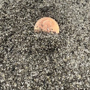 May include: A close-up of a pile of small, clear, glass beads. A copper-colored coin is partially submerged in the beads.
