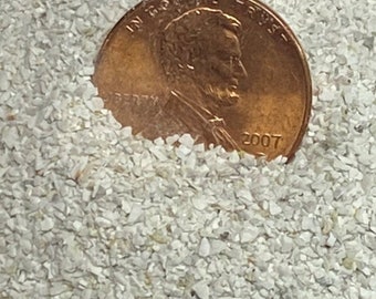 May include: A close-up of white play sand with a penny on top. The penny is dated 2007.